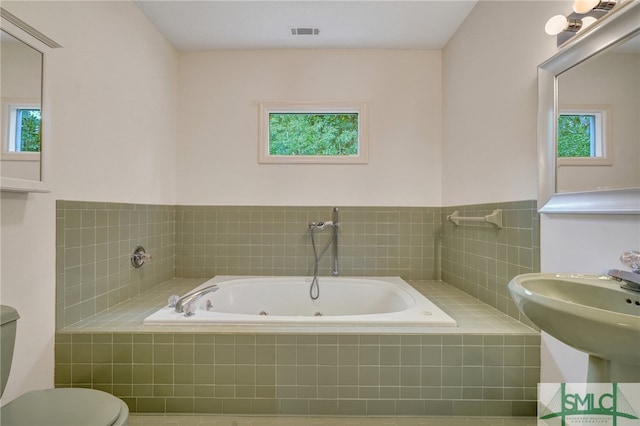 bathroom with toilet, a relaxing tiled tub, and a wealth of natural light