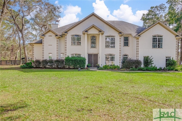 view of front of home with stucco siding, a chimney, fence, and a front yard