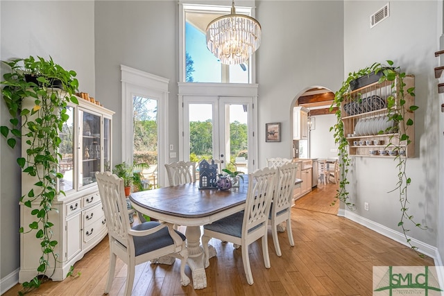 dining room featuring french doors, a towering ceiling, light hardwood / wood-style floors, and a notable chandelier