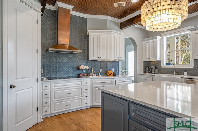 kitchen featuring arched walkways, white cabinetry, a sink, ornamental molding, and wall chimney exhaust hood