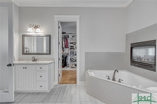 bathroom featuring a multi sided fireplace, a relaxing tiled tub, crown molding, vanity, and hardwood / wood-style flooring