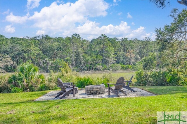 579 Turkey Trot Trl, Richmond Hill, GA 31324 - view of green lawn featuring a fire pit, a wooded view, and a patio area