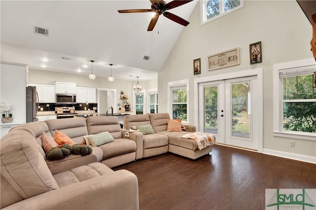 living room featuring ceiling fan with notable chandelier, a healthy amount of sunlight, dark wood-type flooring, and a high ceiling