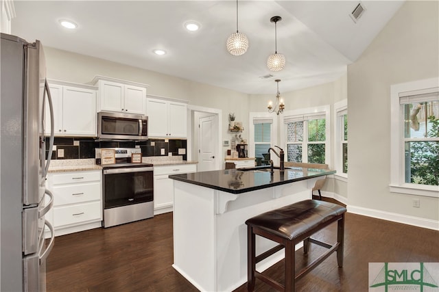 kitchen with appliances with stainless steel finishes, white cabinetry, a kitchen island with sink, decorative light fixtures, and sink