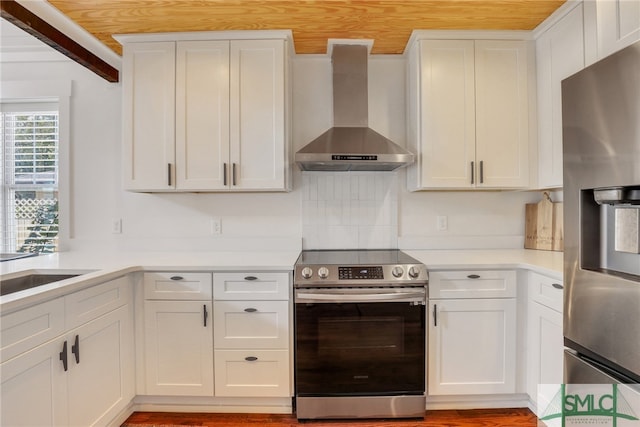 kitchen with decorative backsplash, appliances with stainless steel finishes, white cabinetry, light wood-type flooring, and wall chimney exhaust hood