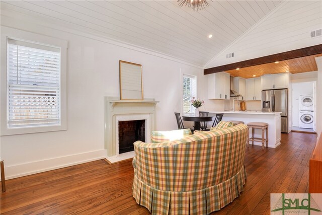 living room featuring lofted ceiling, stacked washer and dryer, dark hardwood / wood-style floors, and wooden ceiling