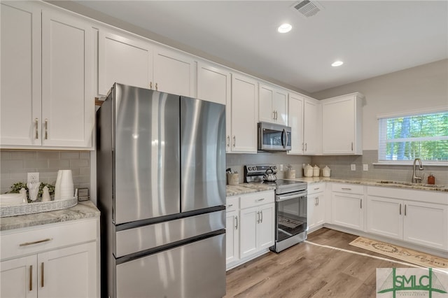 kitchen with sink, stainless steel appliances, light stone counters, light hardwood / wood-style floors, and white cabinets