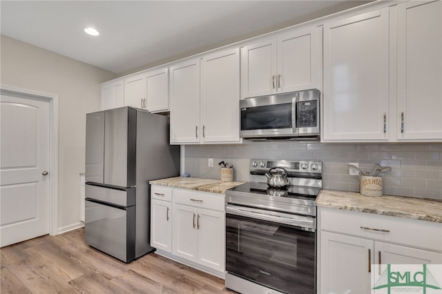 kitchen featuring backsplash, light hardwood / wood-style flooring, light stone countertops, appliances with stainless steel finishes, and white cabinetry