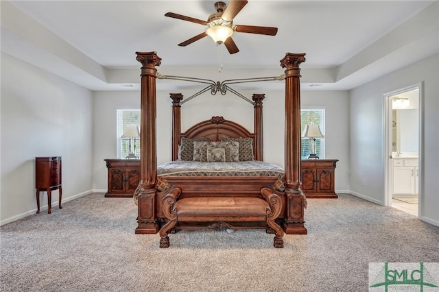 bedroom with light carpet, connected bathroom, a raised ceiling, and ceiling fan