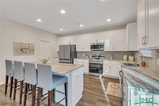 kitchen featuring white cabinetry, a center island, hardwood / wood-style floors, a kitchen bar, and appliances with stainless steel finishes