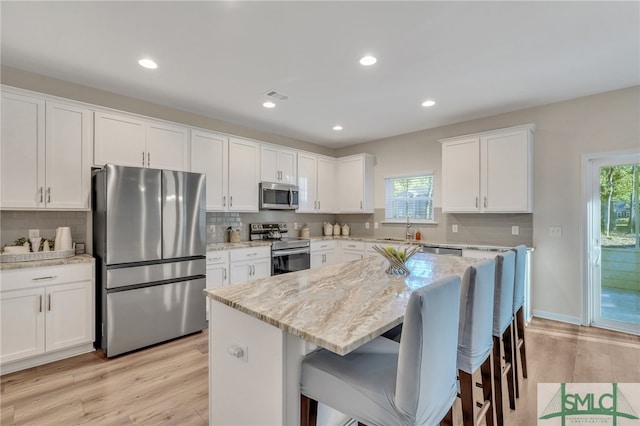 kitchen featuring white cabinets, stainless steel appliances, a kitchen island, and plenty of natural light