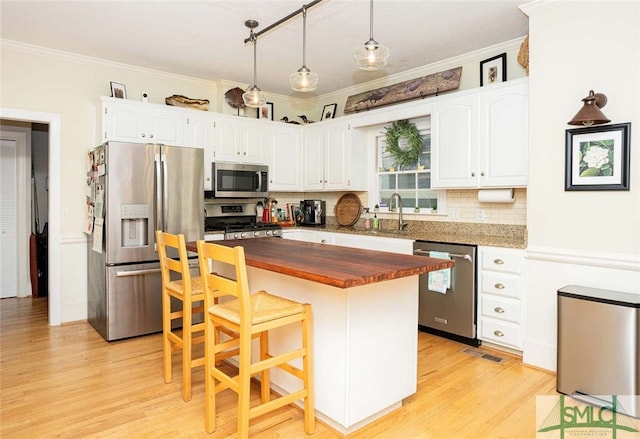 kitchen with wooden counters, stainless steel appliances, hanging light fixtures, and ornamental molding