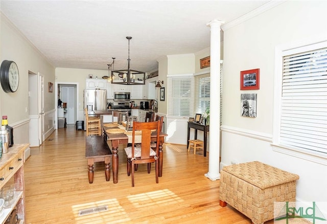 dining area featuring decorative columns, light hardwood / wood-style flooring, a chandelier, and ornamental molding