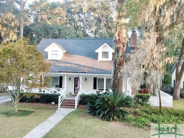 view of front facade with a front lawn, fence, a chimney, a shingled roof, and a porch