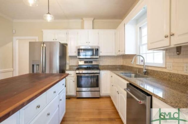 kitchen with white cabinets, appliances with stainless steel finishes, a sink, tasteful backsplash, and ornamental molding