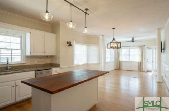 kitchen featuring stainless steel dishwasher, wood finished floors, a sink, butcher block counters, and ornamental molding