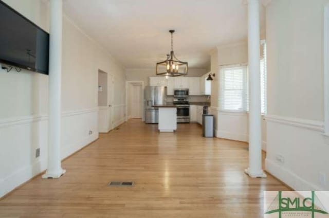 unfurnished dining area featuring baseboards, ornamental molding, light wood finished floors, and a notable chandelier