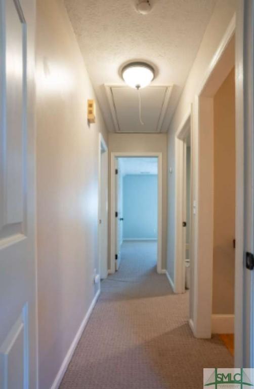 hall with baseboards, attic access, and carpet flooring