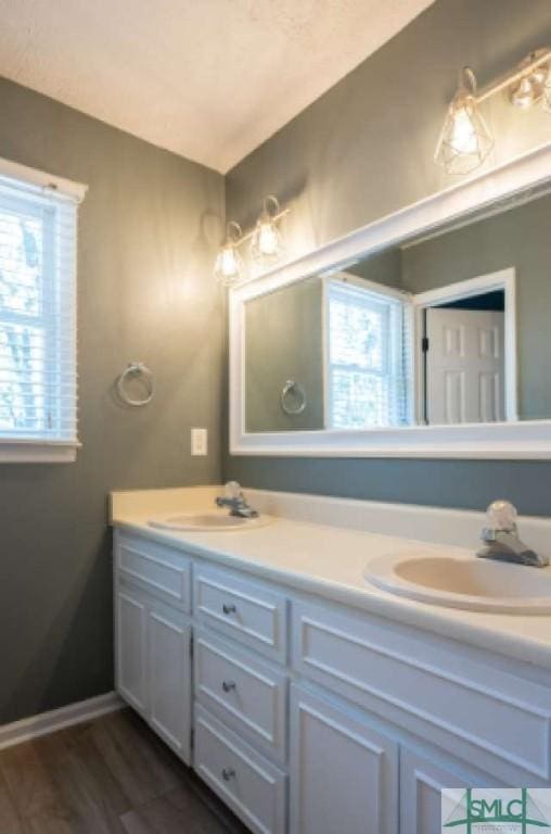 full bathroom featuring a sink, baseboards, double vanity, and wood finished floors
