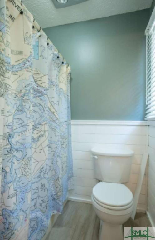 bathroom with a wainscoted wall, curtained shower, toilet, and wood finished floors