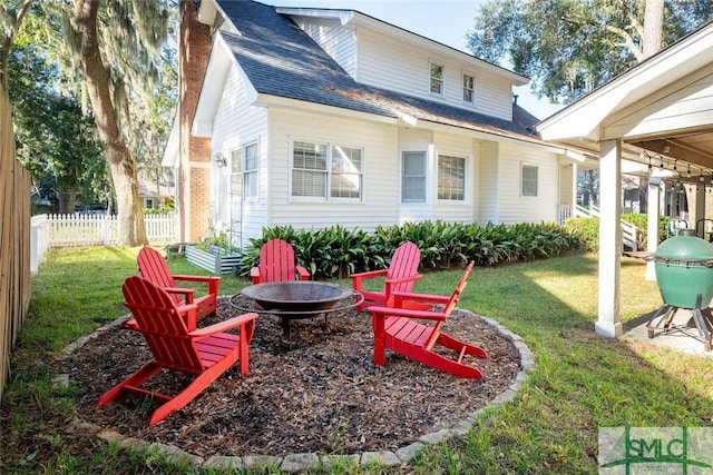rear view of house with fence, roof with shingles, an outdoor fire pit, a chimney, and a yard