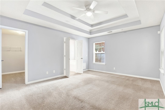 unfurnished bedroom featuring a closet, light carpet, a walk in closet, a tray ceiling, and ceiling fan