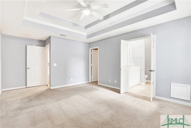 unfurnished bedroom with light colored carpet, ceiling fan, a tray ceiling, and ensuite bath