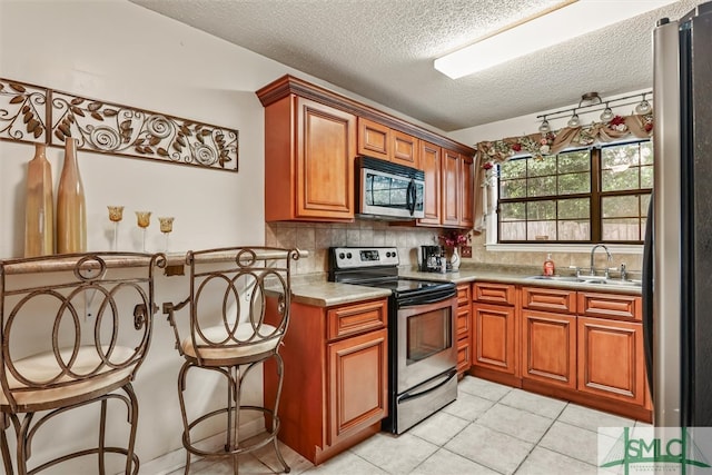 kitchen with sink, decorative backsplash, light tile patterned floors, appliances with stainless steel finishes, and a breakfast bar area