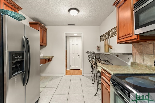 kitchen with decorative backsplash, light tile patterned flooring, stainless steel appliances, and a textured ceiling