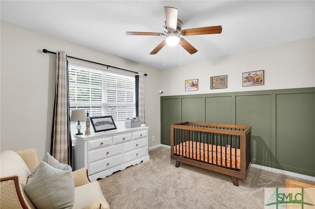 carpeted bedroom with ceiling fan, a textured ceiling, and a crib