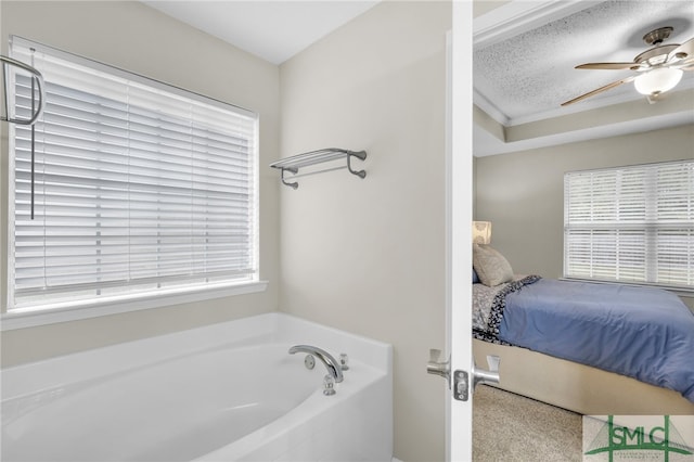 bathroom featuring ceiling fan, a bathtub, a textured ceiling, and plenty of natural light