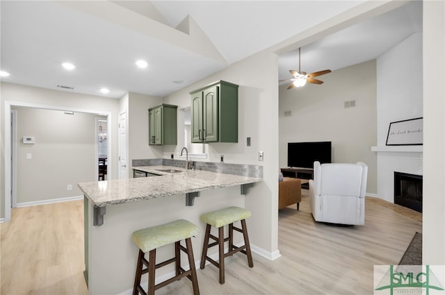 kitchen featuring kitchen peninsula, green cabinets, sink, a kitchen bar, and light wood-type flooring