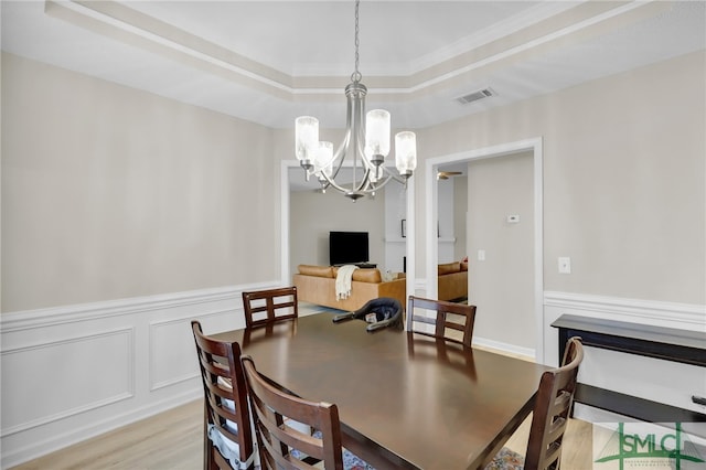 dining room with light hardwood / wood-style floors, crown molding, a raised ceiling, and a chandelier