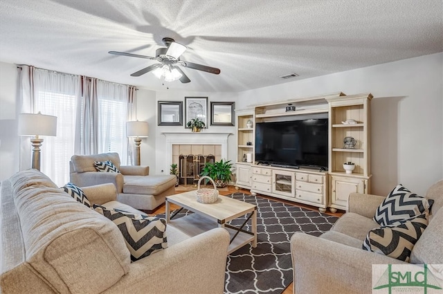 living room with a tiled fireplace, ceiling fan, dark hardwood / wood-style floors, and a textured ceiling