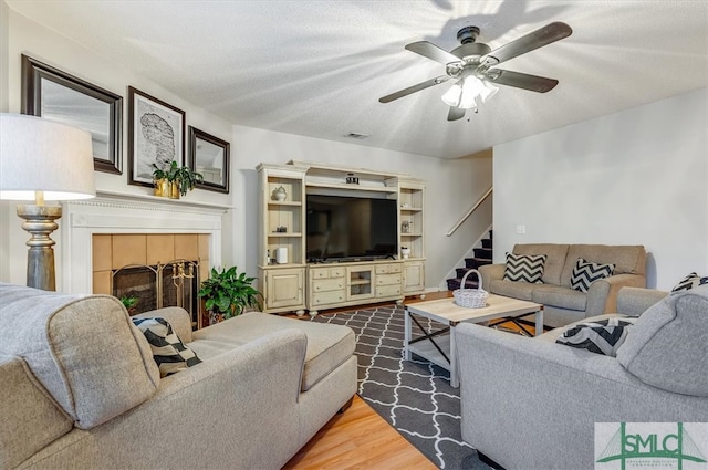 living room featuring a tiled fireplace, ceiling fan, a textured ceiling, and hardwood / wood-style flooring