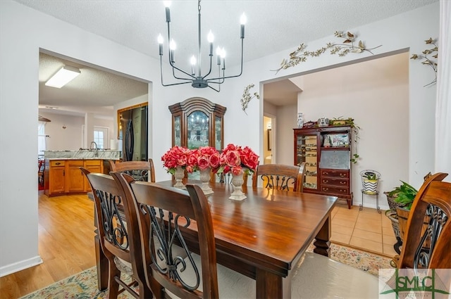 dining area featuring light wood-type flooring, a textured ceiling, and an inviting chandelier