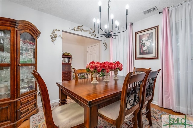 dining space with plenty of natural light, light wood-type flooring, a textured ceiling, and a chandelier