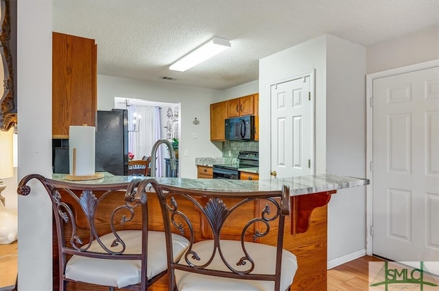 kitchen with black appliances, sink, a textured ceiling, tasteful backsplash, and light hardwood / wood-style floors