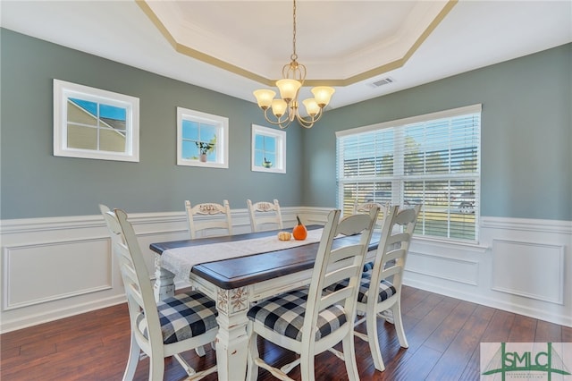 dining area featuring dark wood-type flooring, a raised ceiling, and a chandelier