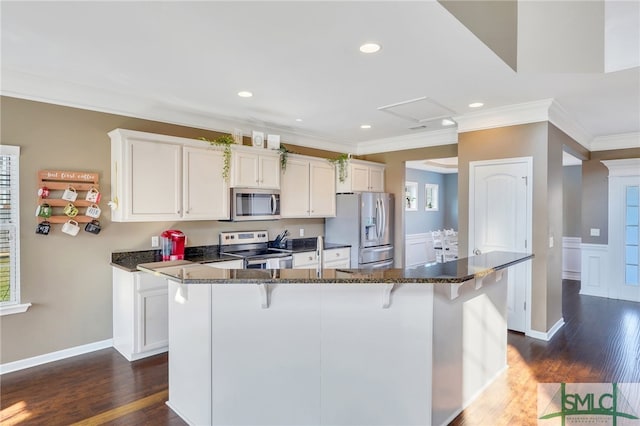 kitchen with stainless steel appliances, dark stone counters, white cabinets, dark wood-type flooring, and ornamental molding