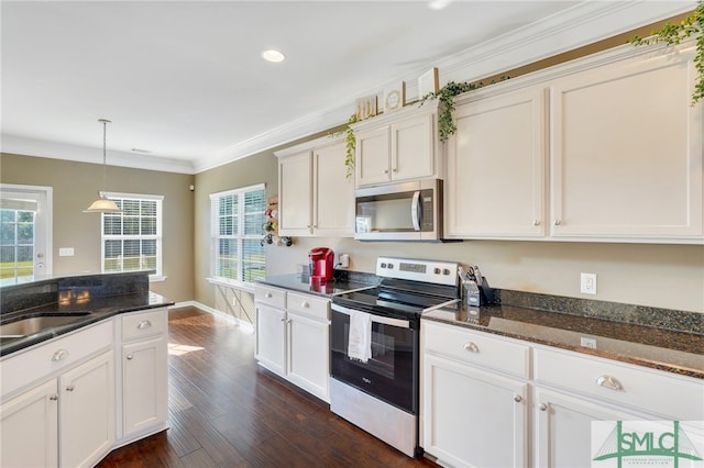 kitchen featuring dark stone counters, ornamental molding, stainless steel appliances, dark wood-type flooring, and decorative light fixtures