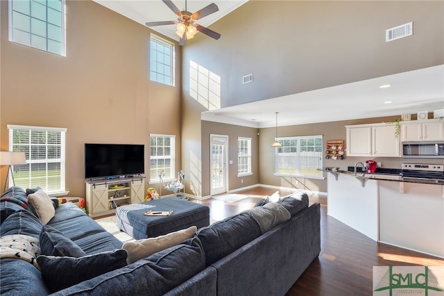 living room with dark wood-type flooring, ceiling fan, a healthy amount of sunlight, and a high ceiling