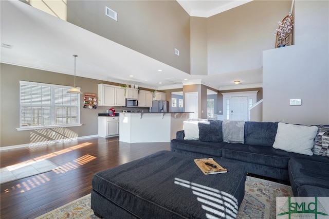 living room featuring dark wood-type flooring, crown molding, and a towering ceiling