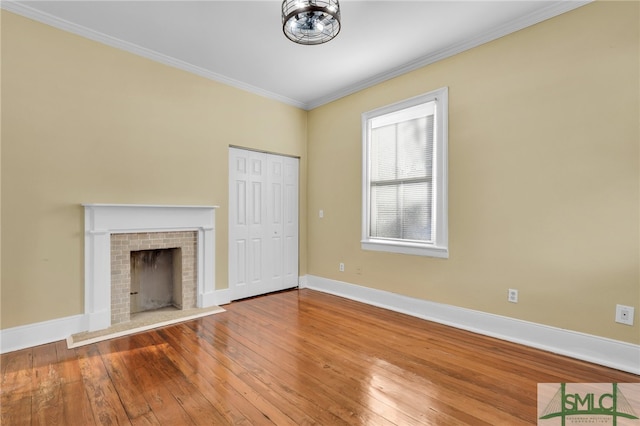 unfurnished living room with hardwood / wood-style floors, crown molding, and a brick fireplace