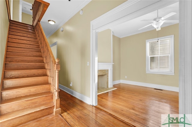 stairway featuring ceiling fan, wood-type flooring, and ornamental molding