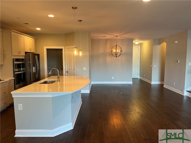 kitchen with sink, an island with sink, hanging light fixtures, stainless steel appliances, and dark wood-type flooring