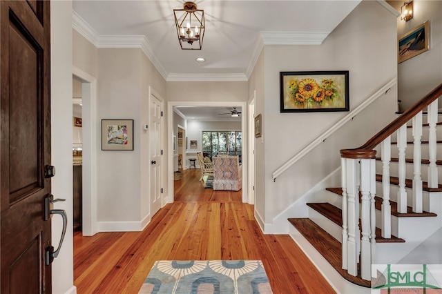 foyer entrance with ornamental molding, light hardwood / wood-style flooring, and ceiling fan with notable chandelier