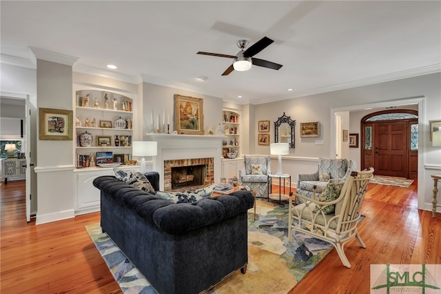 living room featuring light hardwood / wood-style flooring, ceiling fan, a fireplace, and crown molding