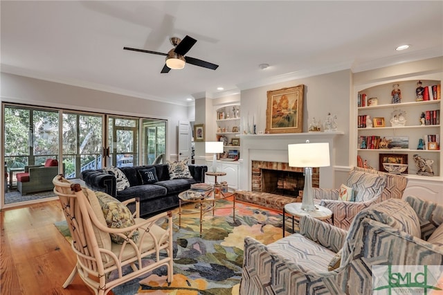 living room with a fireplace, crown molding, built in shelves, light hardwood / wood-style floors, and ceiling fan