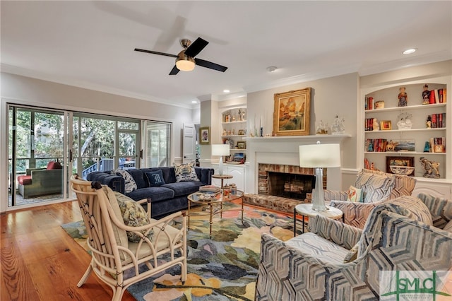 living room with ceiling fan, light hardwood / wood-style flooring, ornamental molding, a fireplace, and built in shelves